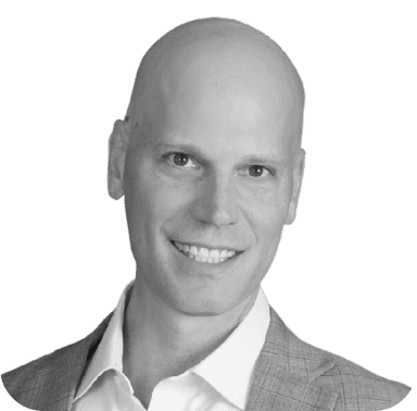 A black and white portrait of a bald man smiling, dressed in a business suit.