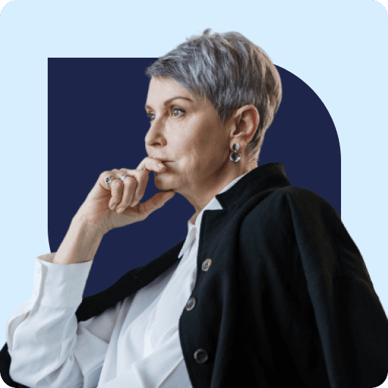 Mature woman with short gray hair and earrings, dressed in a black blazer and white blouse, thoughtfully touching her chin.