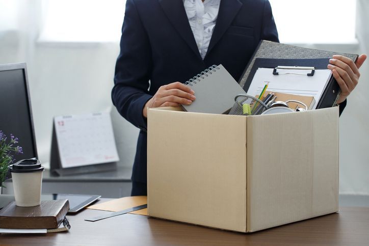 woman standing behind desk with box filled with her stuff in front of her