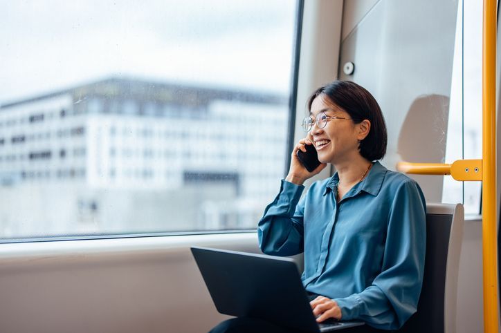 Businesswoman in public transport. Using smart phone and laptop. Sitting next to window. Commuting.